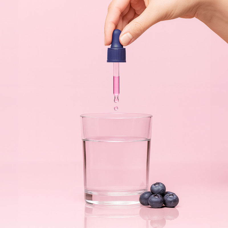 Hand using a dropper to add liquid into a glass with blueberries on a pink background